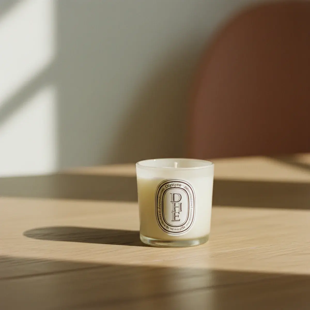 A real cream cashmere jumper folded with a sprig of dried lavender on top, beside a small leather notebook cover, a Diptyque candle, and a handwritten note on a wooden surface