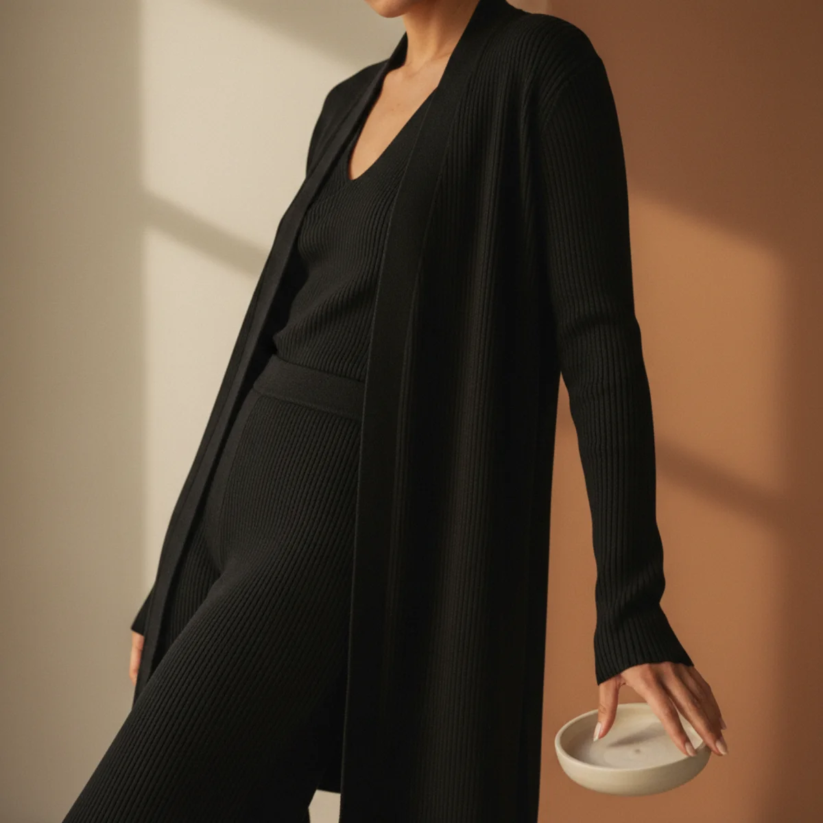 Faceless waist-up shot of an all-black ribbed knit co-ord with a longline cardigan and matching wide-leg trousers