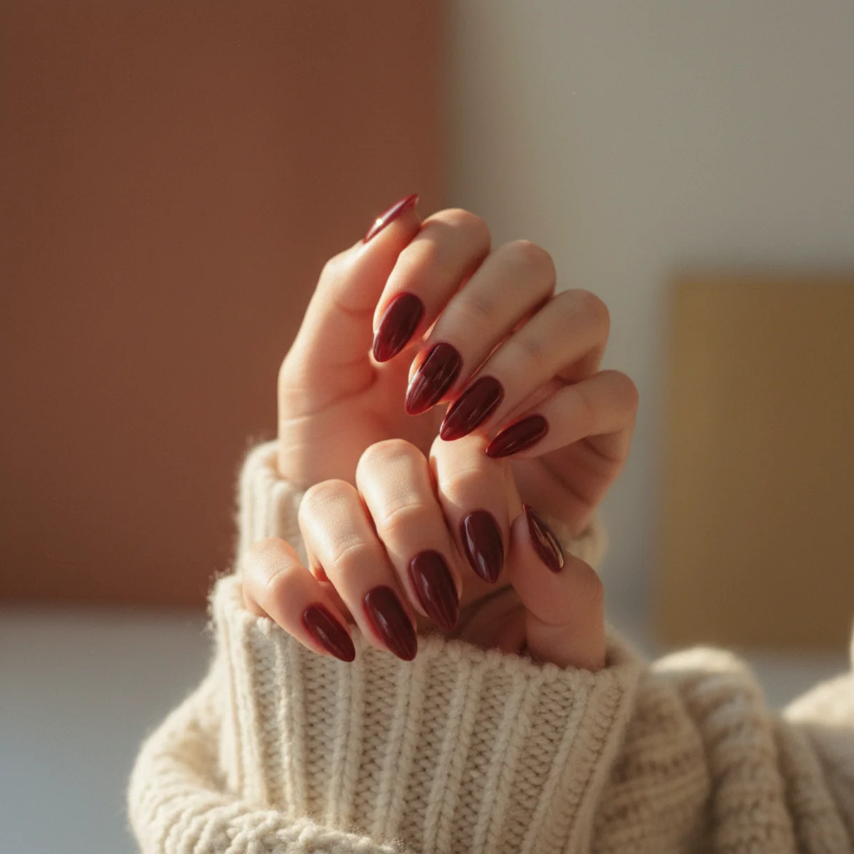 Deep glossy red-wine burgundy almond nails on a cream knit fabric