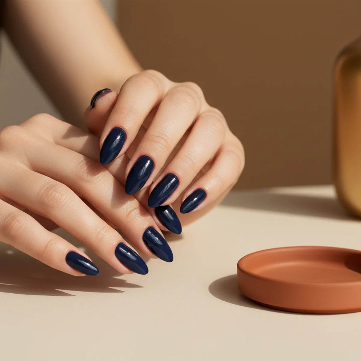 Deep glossy midnight-navy almond nails on a cream surface