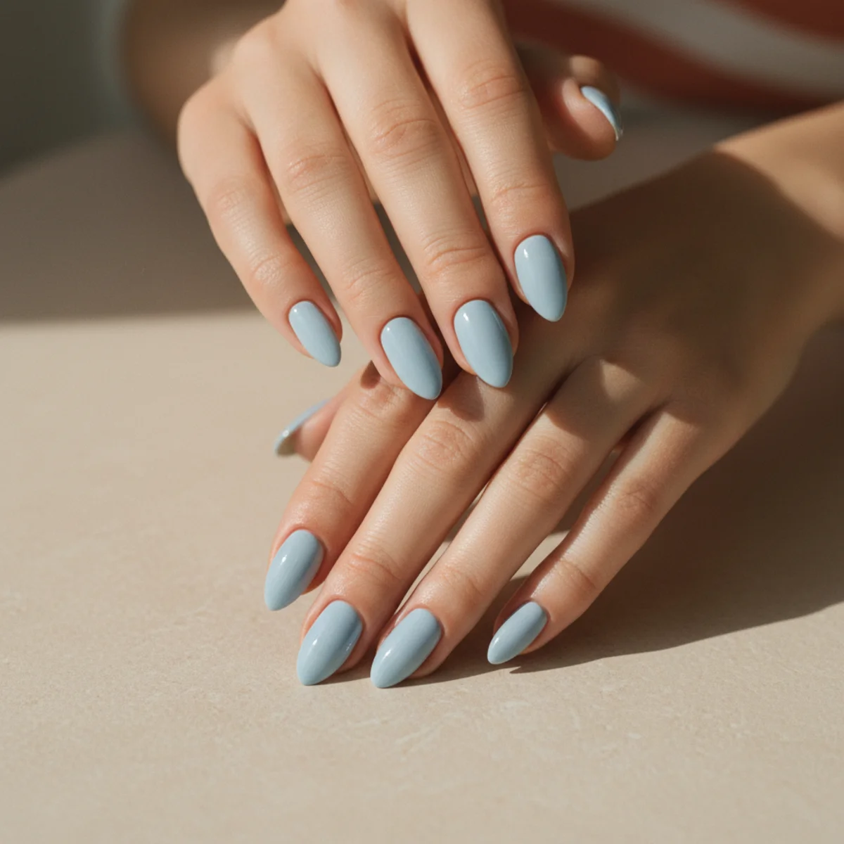 Soft creamy powder-blue almond nails on a pale neutral surface