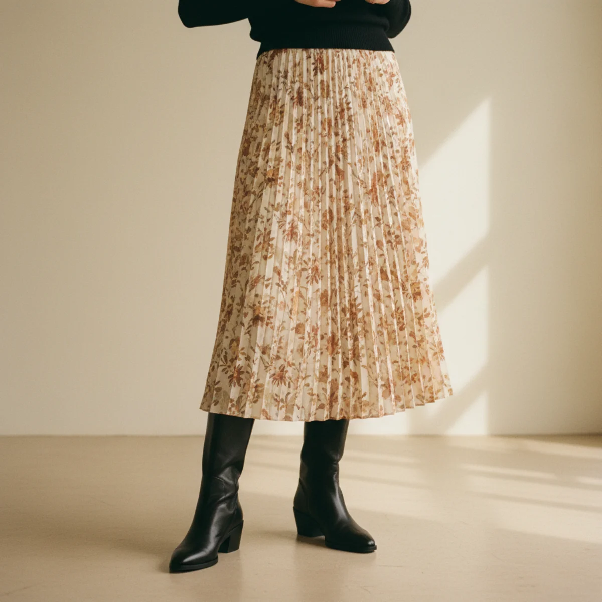 Waist-down shot of black ankle boots with a flowing floral midi skirt and the hem of a slim black polo neck