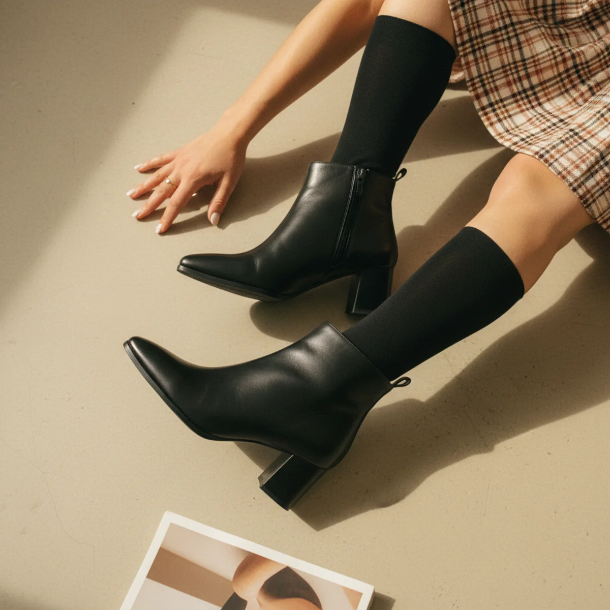 Waist-down editorial of black heeled ankle boots with black knee socks and a short plaid mini dress