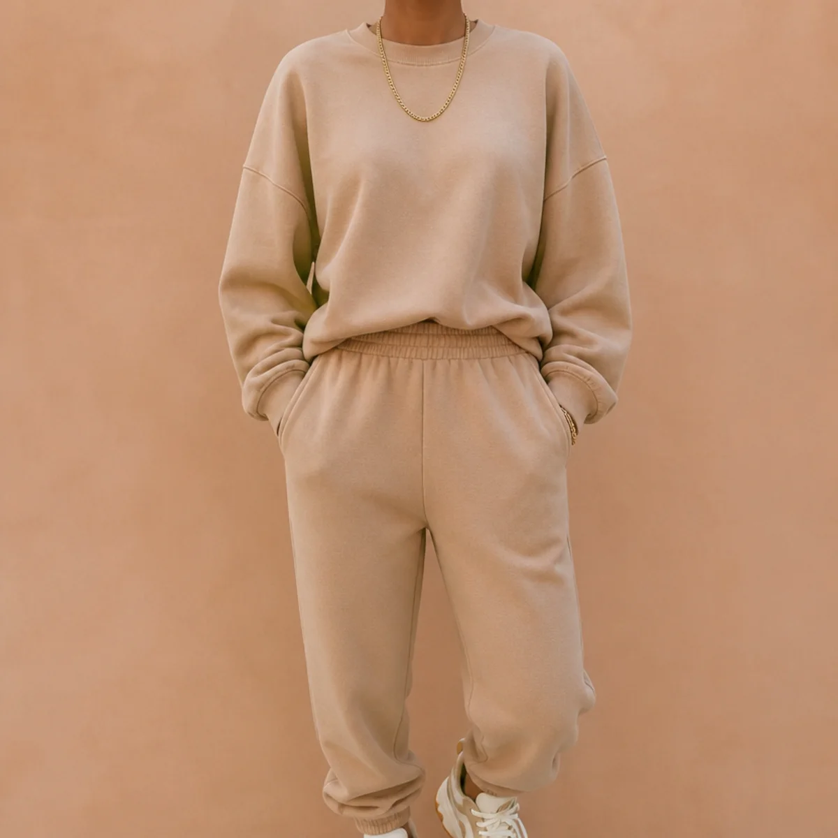 Faceless waist-up shot of a tonal sweat set styled with simple gold jewellery and trainers