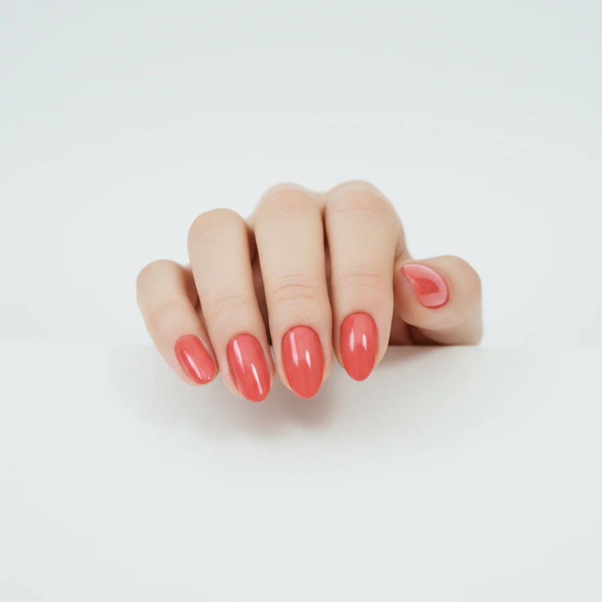 Short almond nails in a vivid warm watermelon pink on a bright white surface