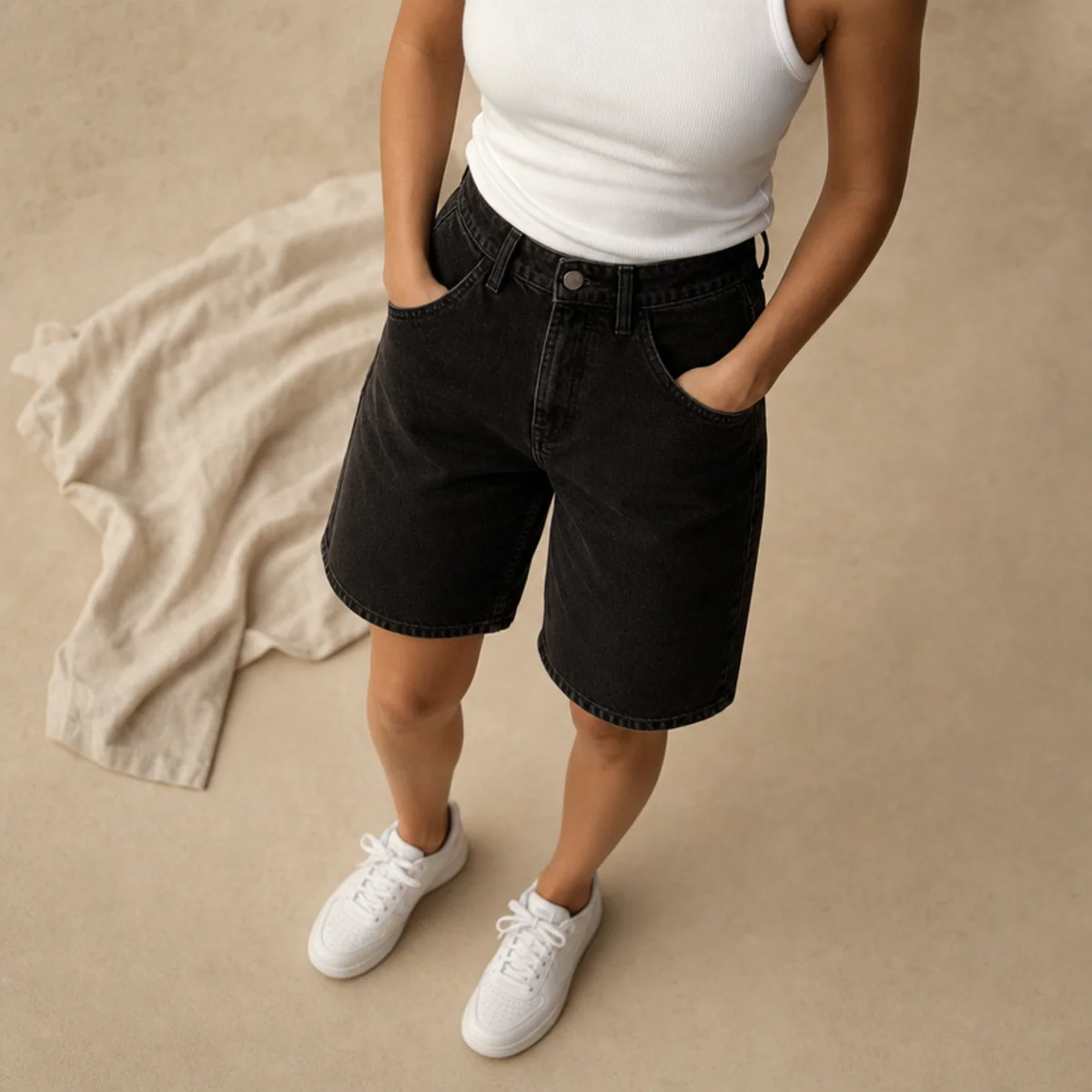 Faceless waist-down shot of black denim jorts with a tucked white tank and white sneakers