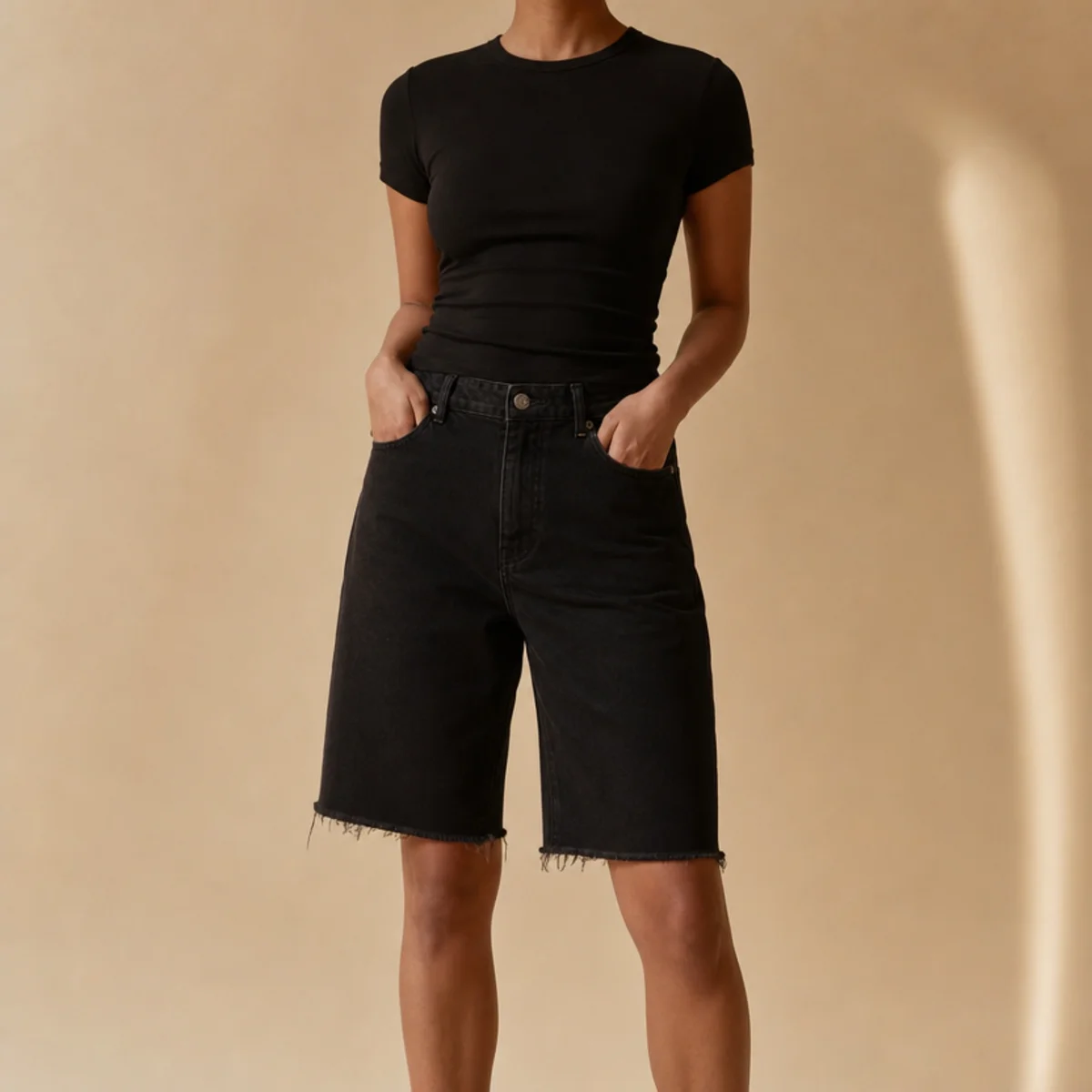Faceless waist-up shot of an all-black outfit with a fitted top and black denim jorts
