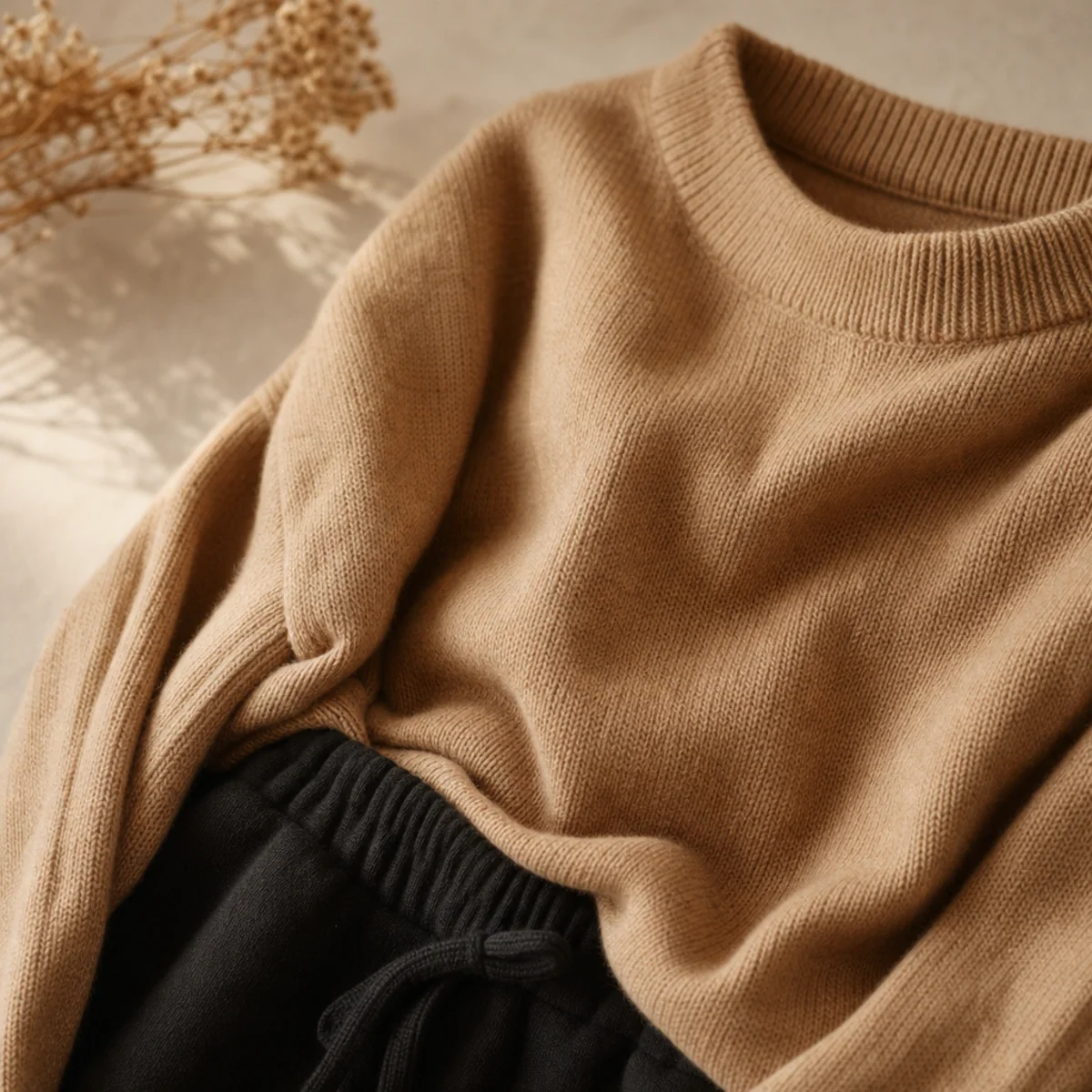 Faceless waist-up shot of an oversized camel knit jumper with black sweatpants