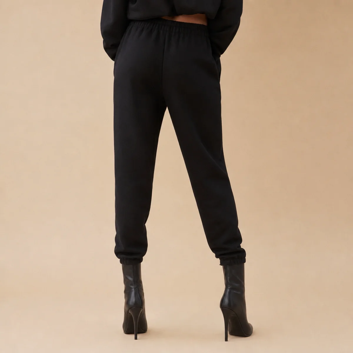 Faceless waist-down shot of slim black sweatpants tucked into sleek black heeled boots