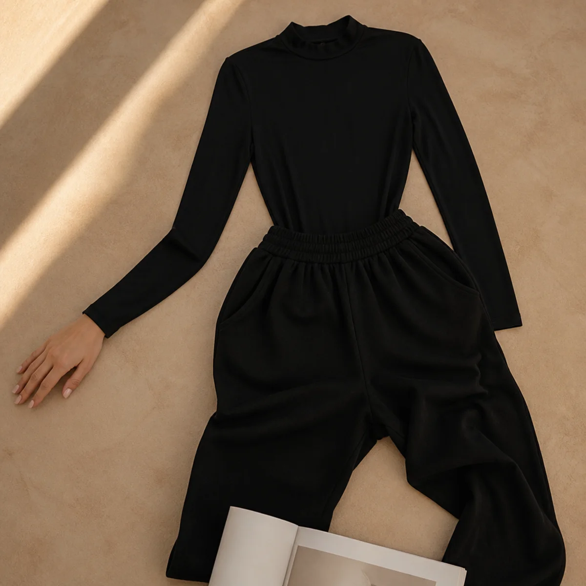 Faceless waist-up shot of a fitted black bodysuit tucked into high-waisted black sweatpants
