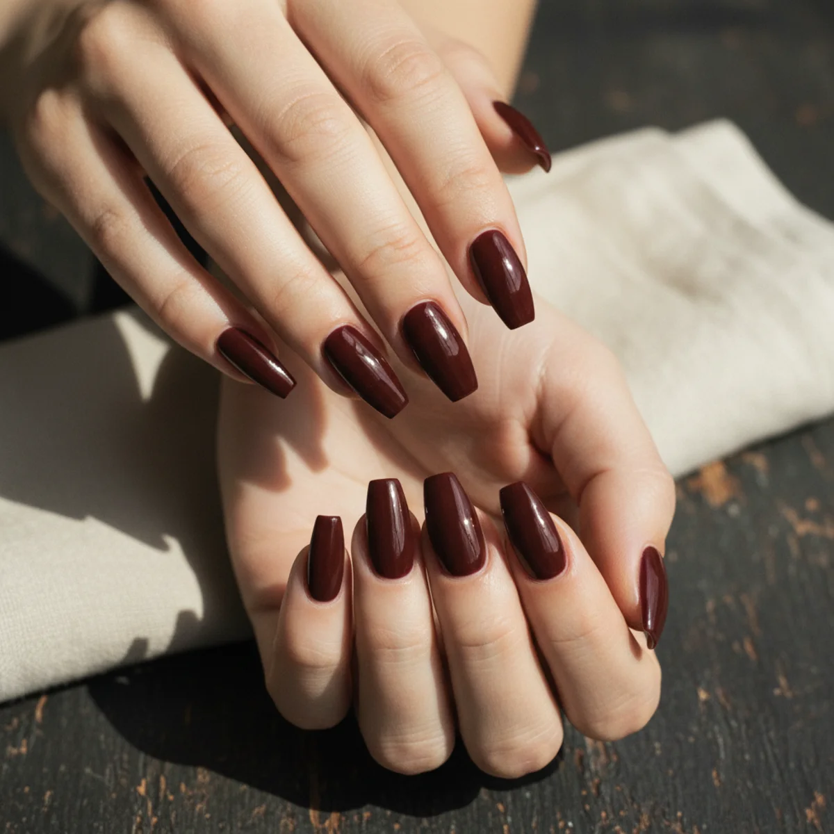 Long coffin nails in a deep glossy burgundy on a dark textured background