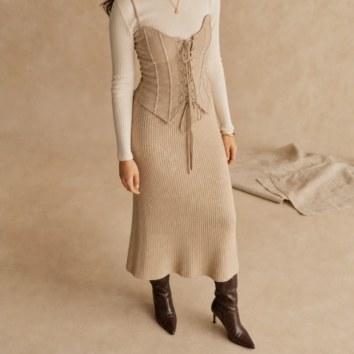 Faceless full-length shot of a corset top over a long-sleeve with a knit midi skirt and boots
