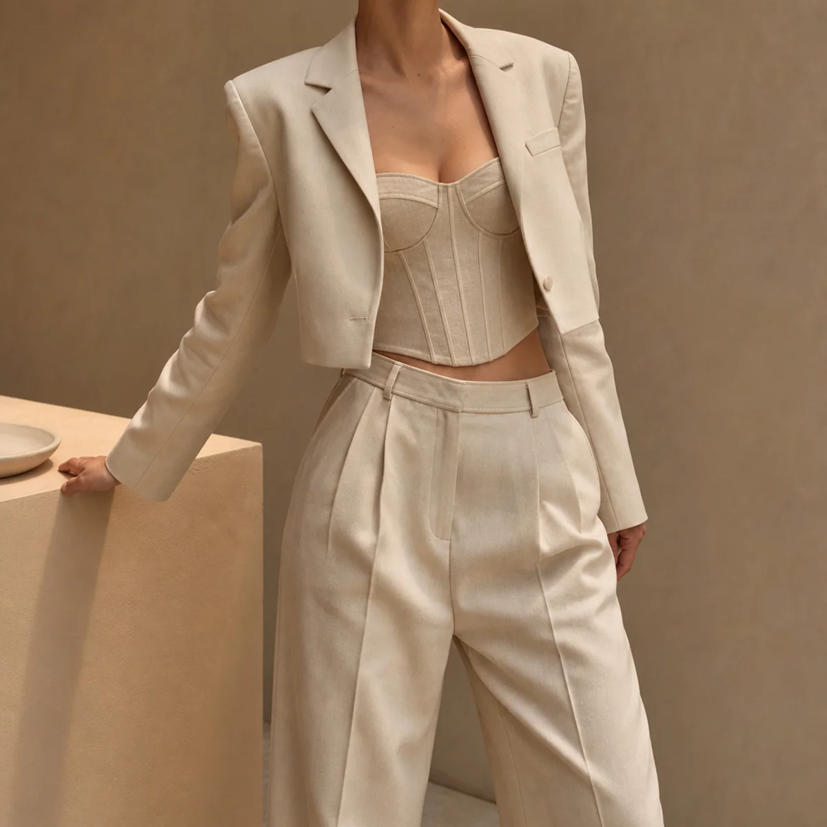 Faceless waist-up shot of a corset top under a cropped blazer with high-waisted trousers