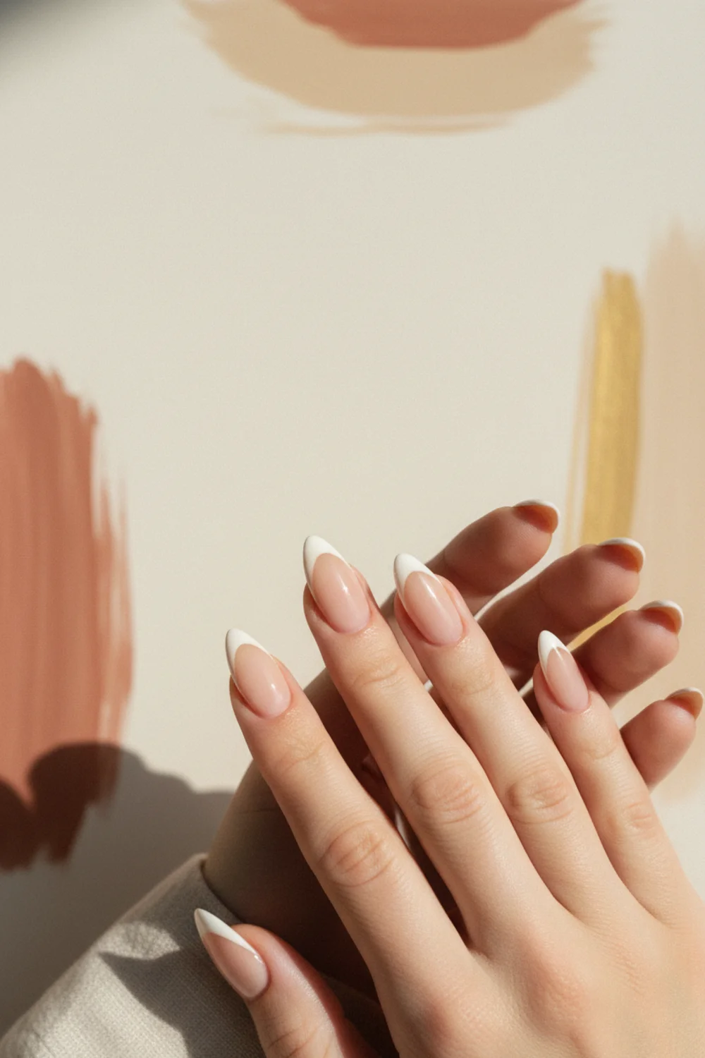 Almond nails with a slim modern warm-white French tip on a pale cream linen surface