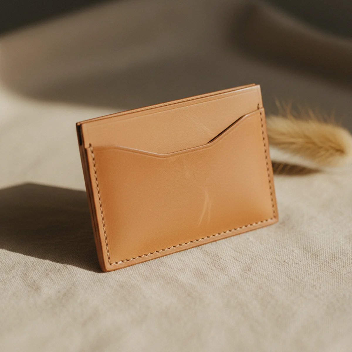 Flat-lay of a slim minimalist tan leather card holder and small fold wallet on a warm neutral surface