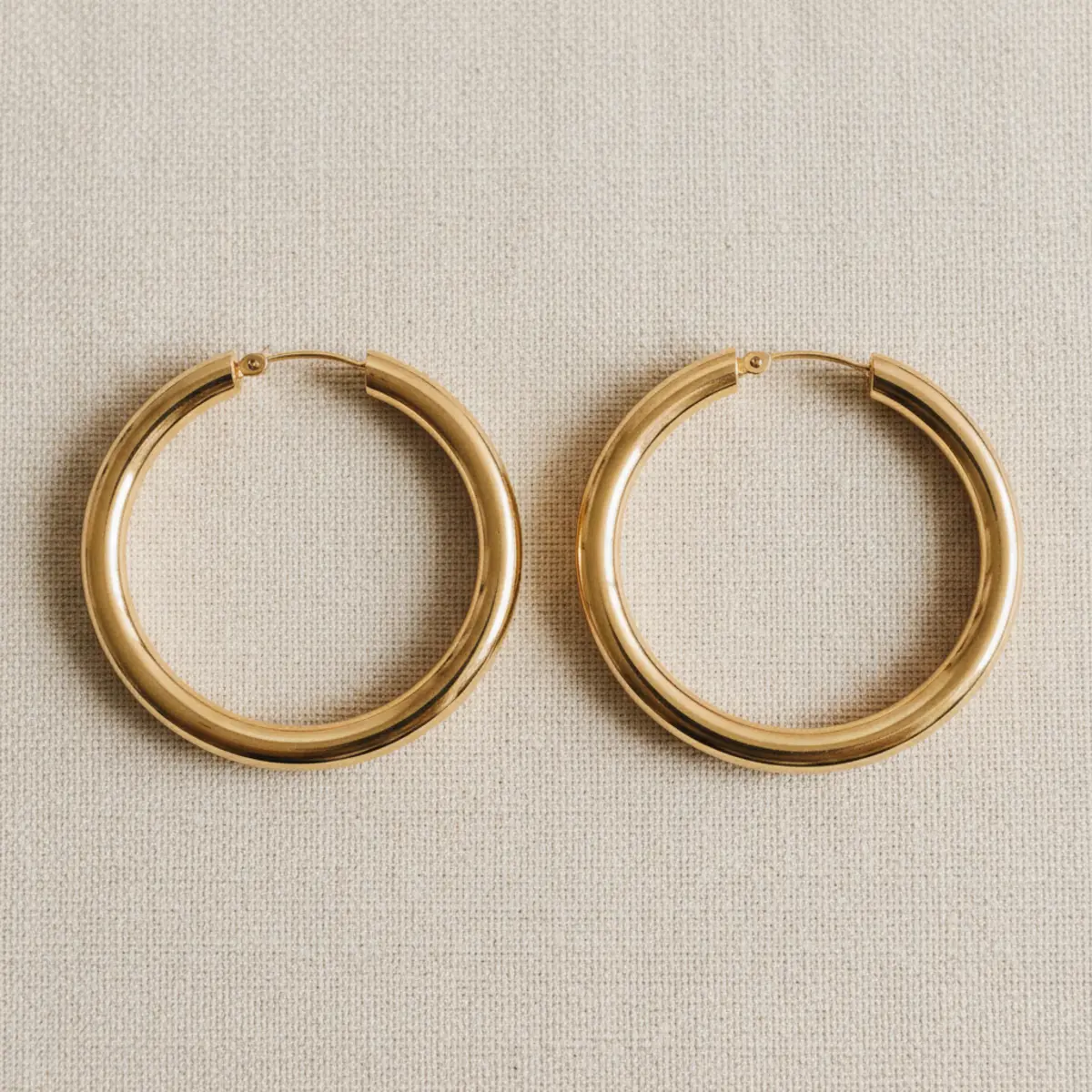 Flat-lay of three pairs of gold hoop earrings in graduating sizes on a velvet-lined jewellery box on cream linen