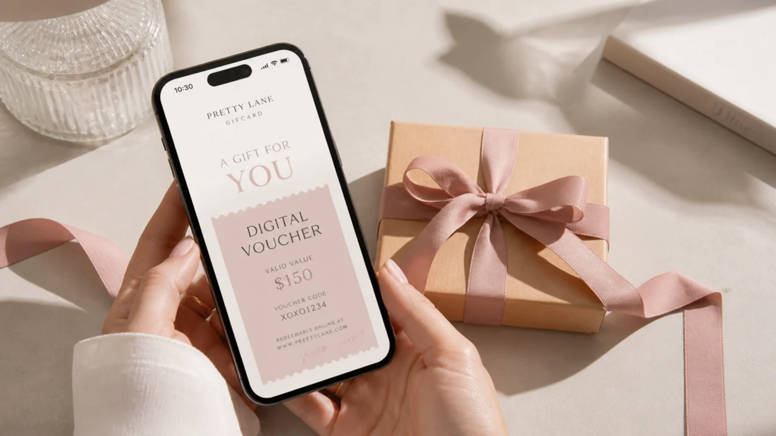 Faceless shot of a phone showing a digital voucher beside a small ribbon-tied parcel on a neutral surface