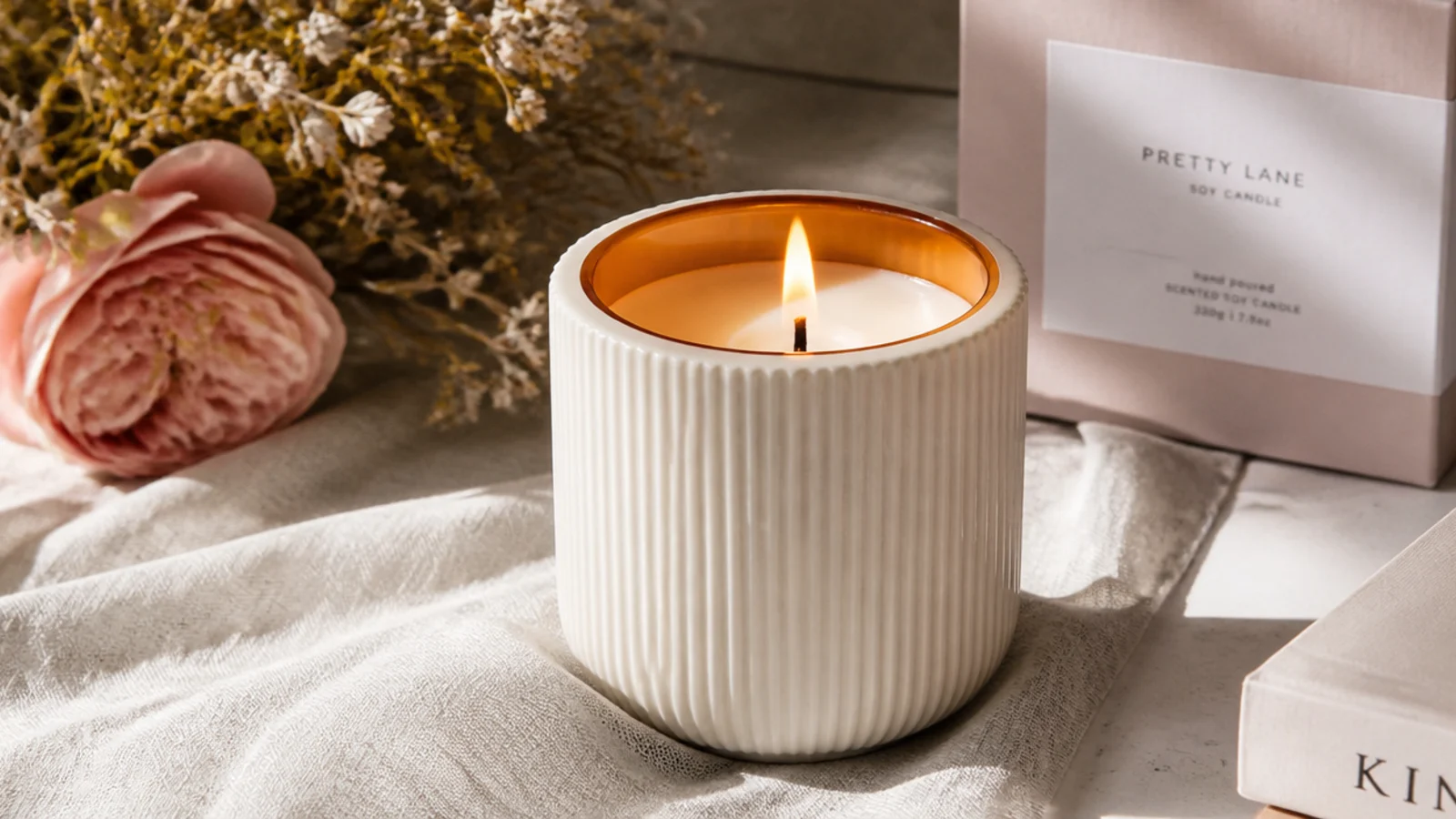 Faceless close-up of an amber soy candle in a ribbed cream jar on a linen surface