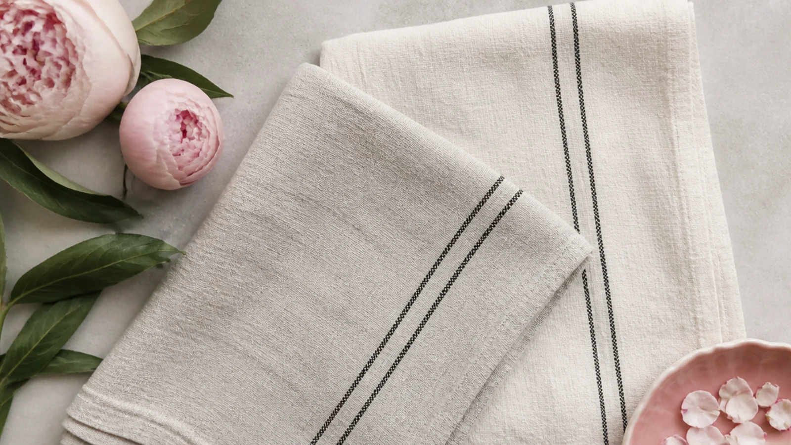 Faceless flat-lay of two washed-linen tea towels with a thin charcoal stripe