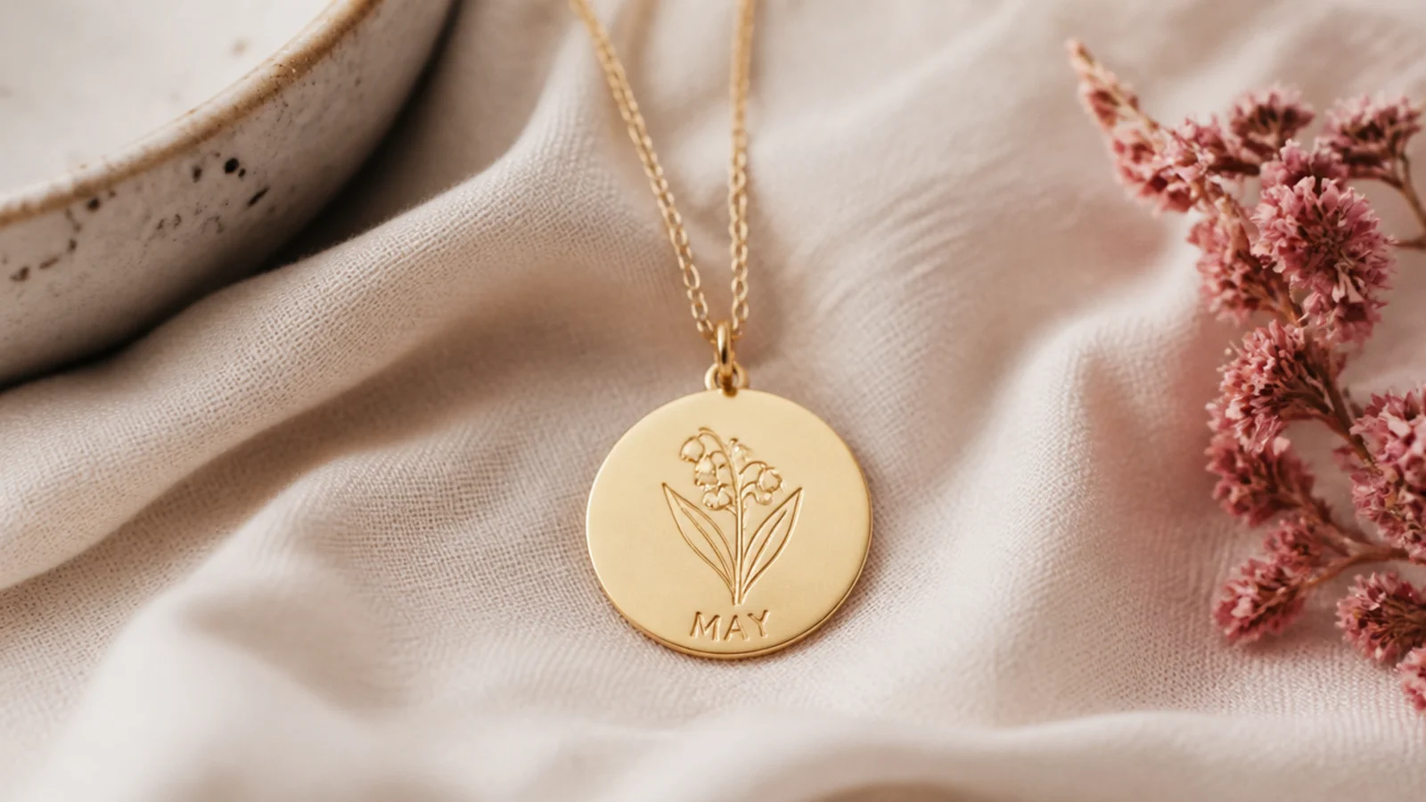 Faceless close-up of a delicate gold pendant engraved with a birth-month flower on a fine chain