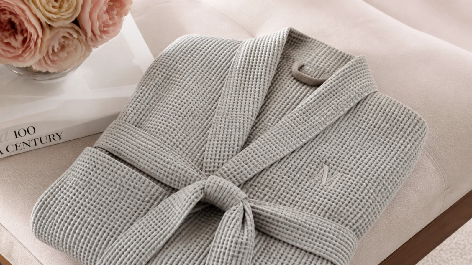 Faceless shot of a folded waffle-knit robe in stone gray with a small embroidered initial on the chest