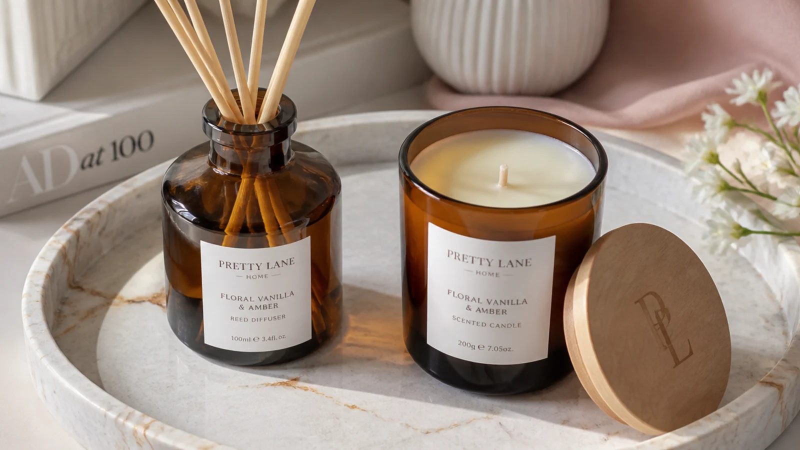 Faceless flat-lay of a reed diffuser and matching candle in amber glass on a marble tray