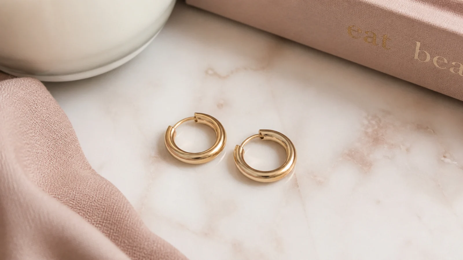 Faceless close-up of small solid gold hoop earrings on a marble surface
