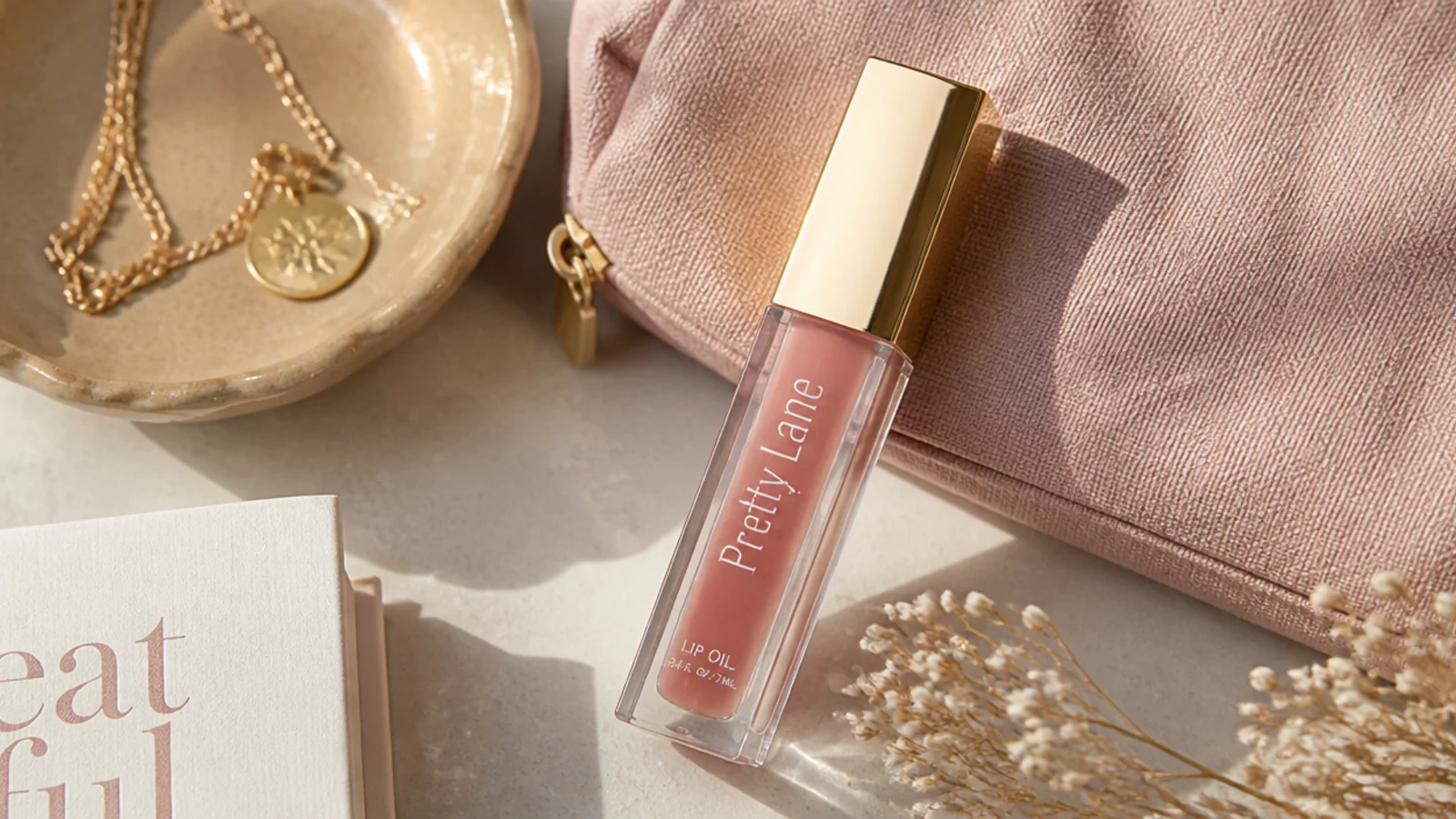 Faceless close-up of a clear tinted lip oil tube in a soft rosewood shade