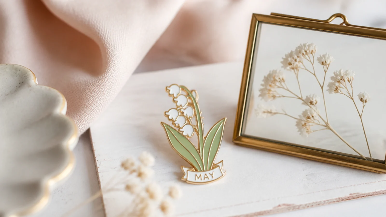 Faceless close-up of a birth-flower enamel pin beside a small pressed-flower frame