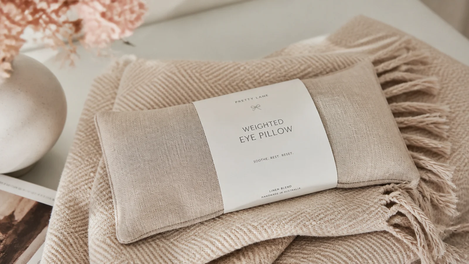Faceless close-up of a linen weighted eye pillow resting on a folded throw