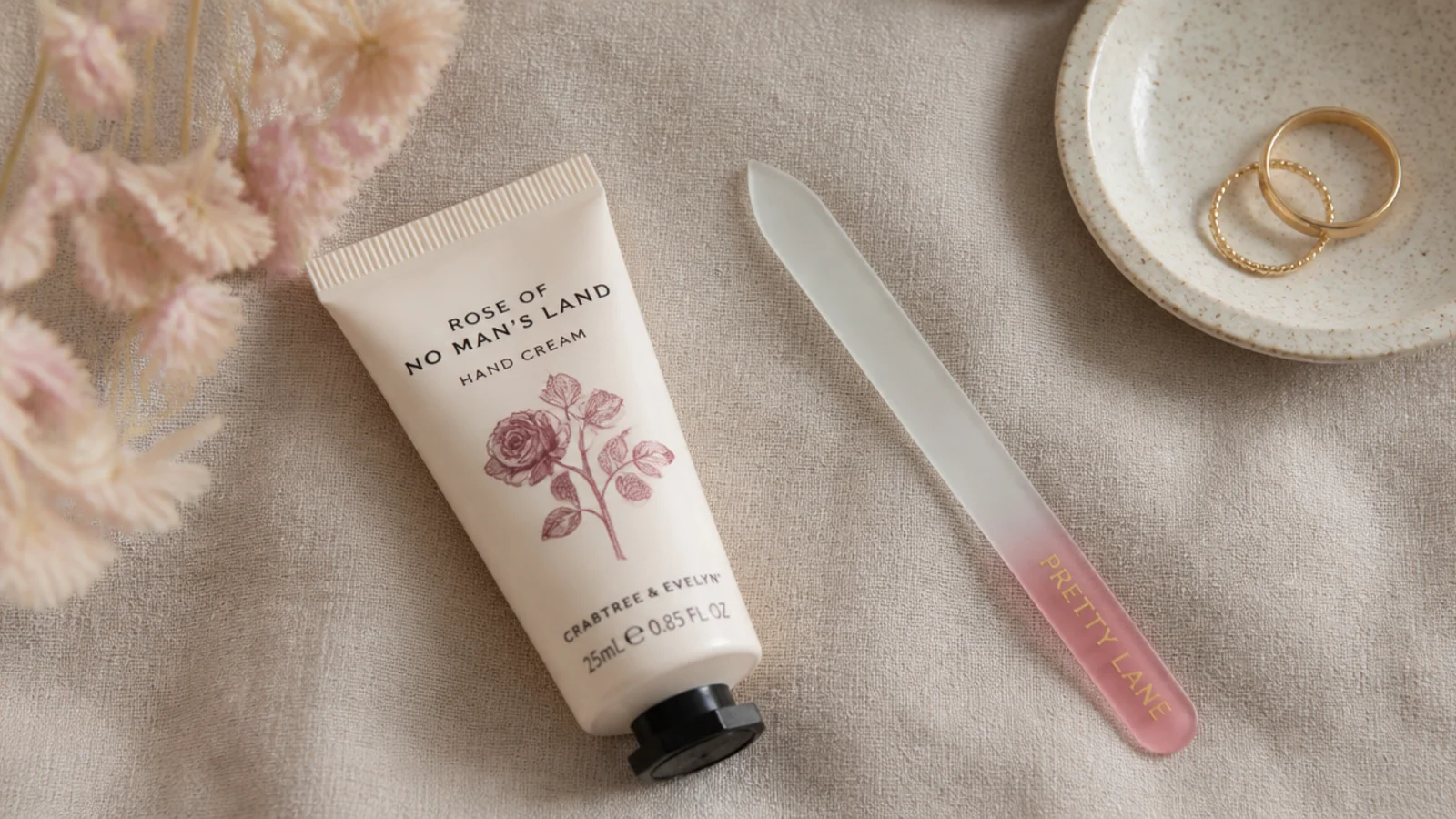 Faceless flat-lay of a hand cream tube beside a glass nail file on linen