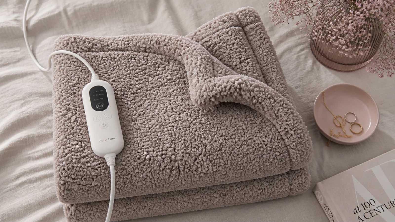 Faceless flat-lay of a folded taupe sherpa electric heated throw with its controller on linen