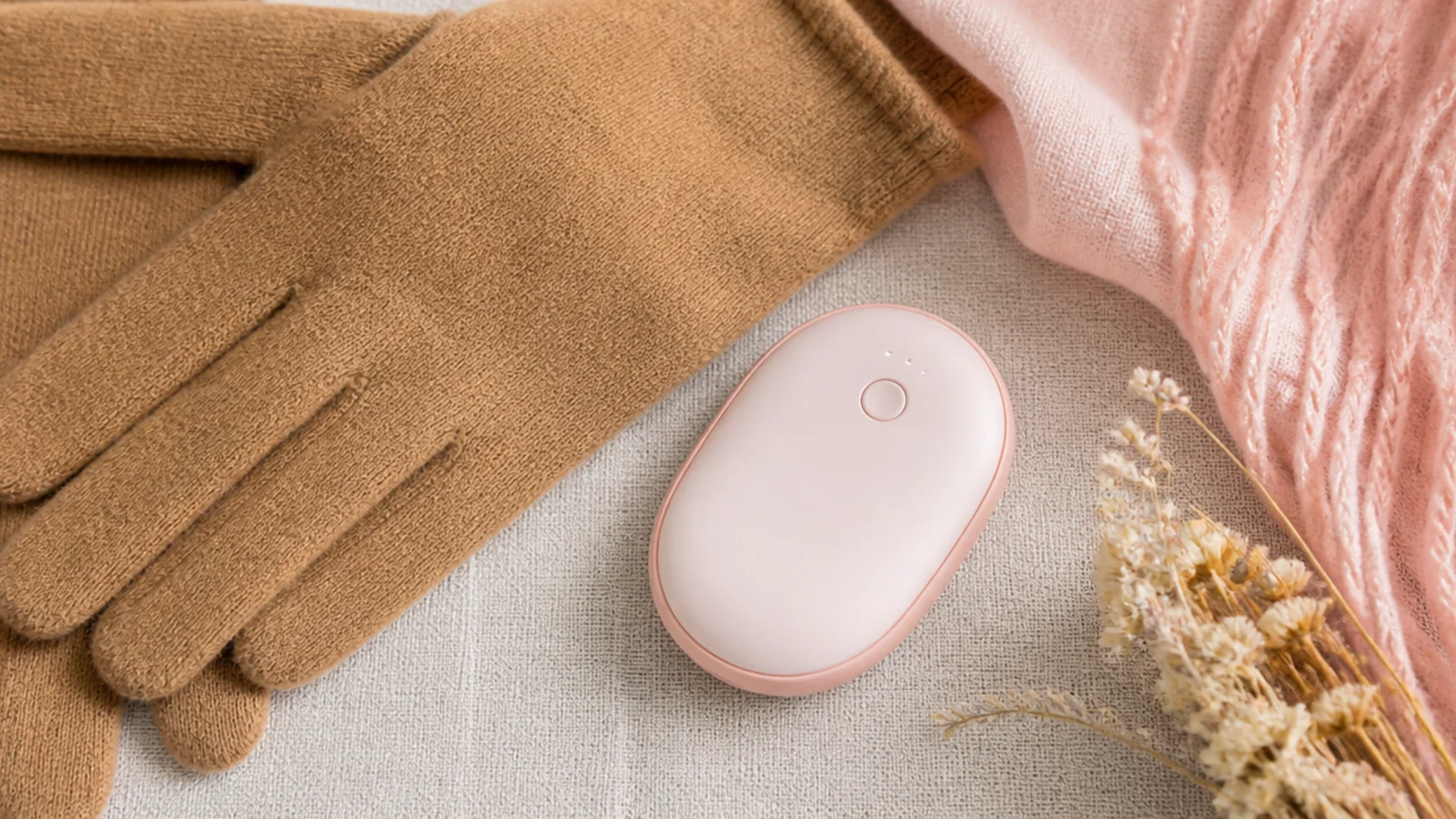 Faceless flat-lay of a small oval rechargeable hand warmer beside camel gloves on linen