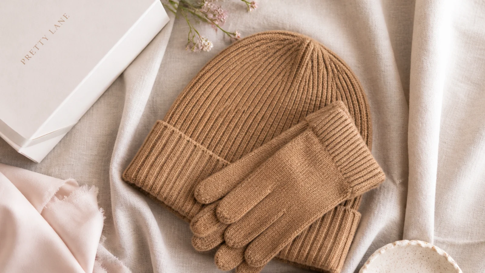 Faceless flat-lay of a camel cashmere ribbed beanie and matching gloves folded on linen