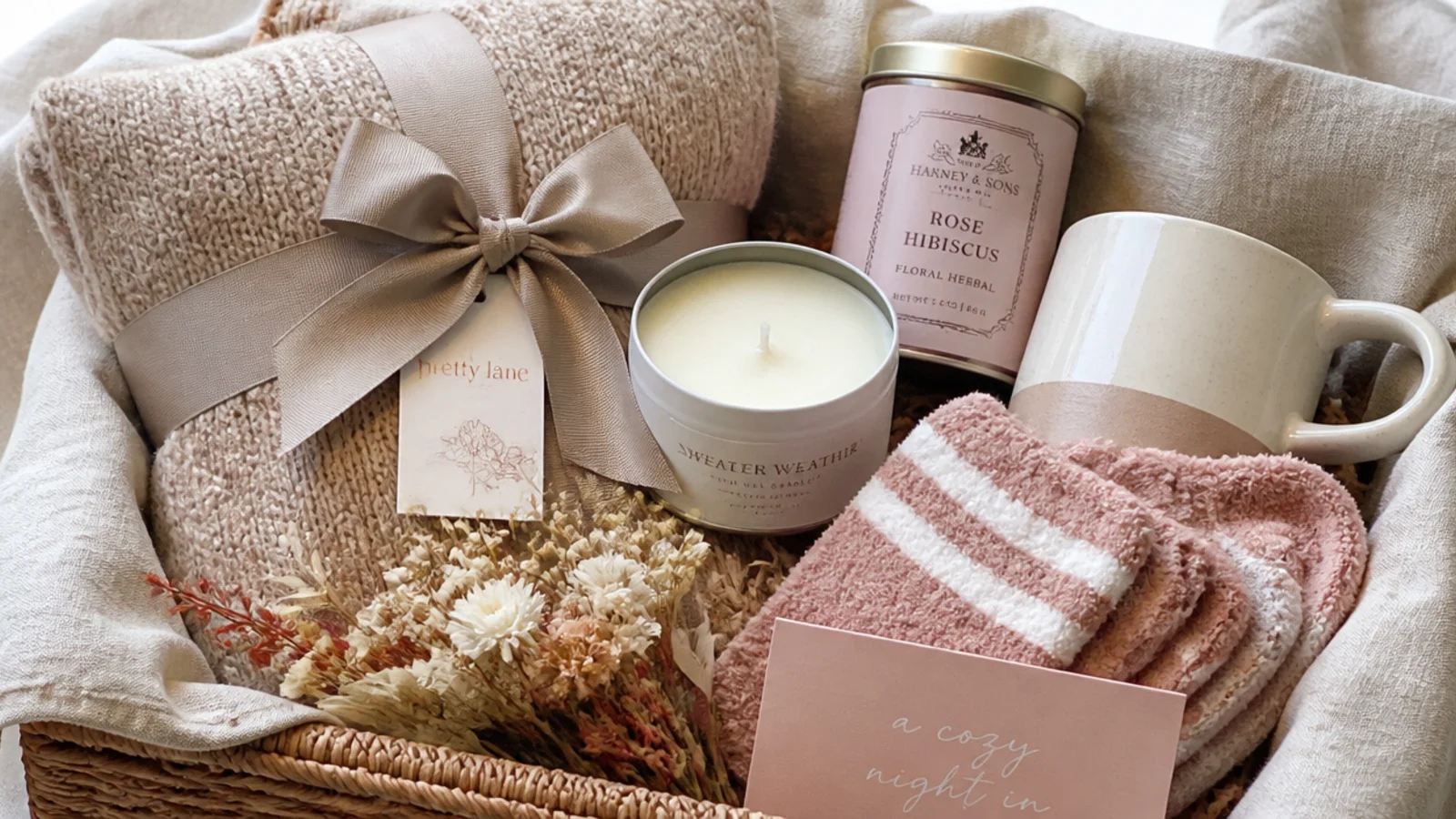 Faceless flat-lay of an assembled cozy night in gift box with a throw, candle, socks and tea in a linen-lined basket