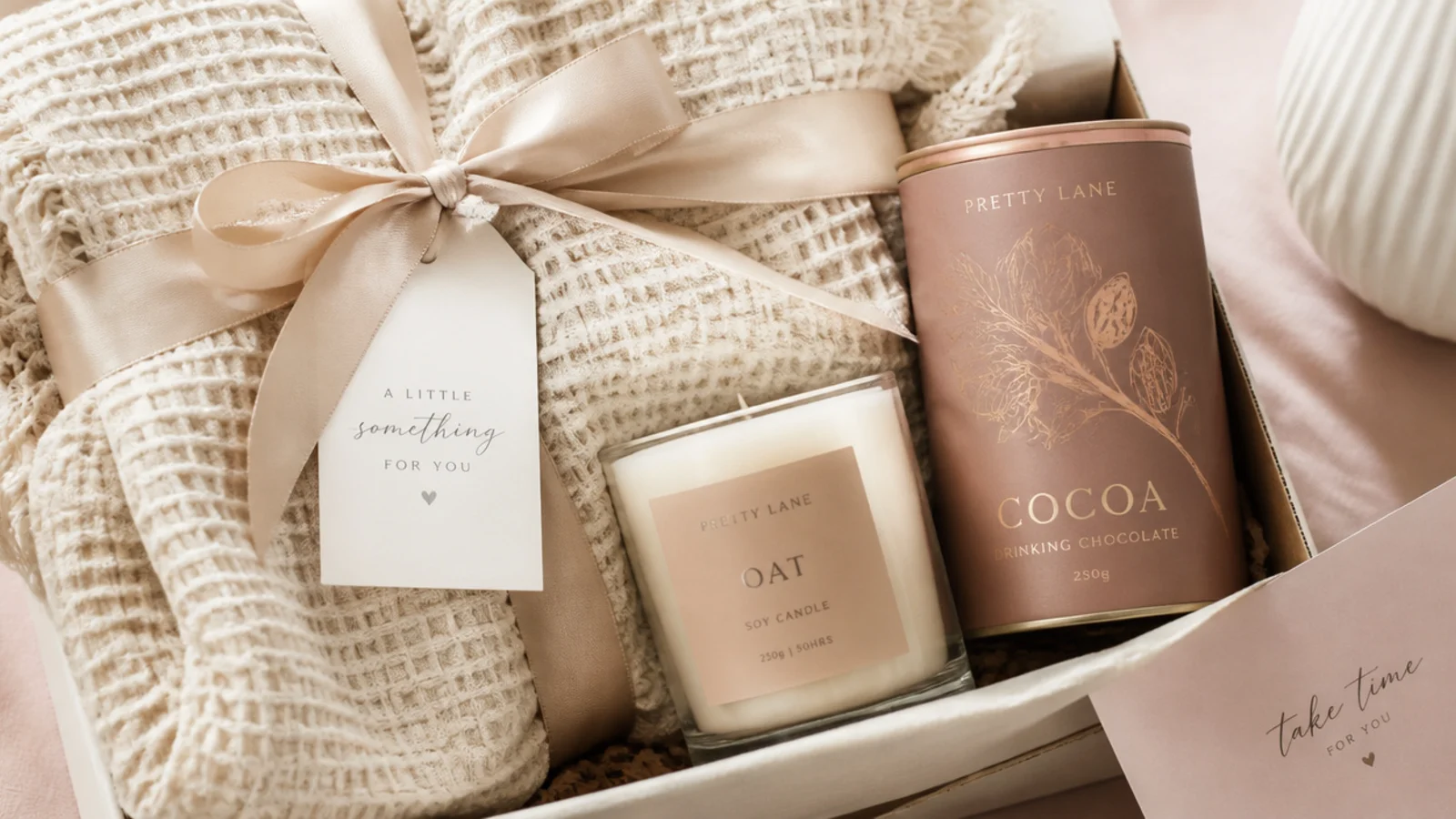 Faceless flat-lay of a cozy night in gift hamper with cream waffle throw, oat soy candle and cocoa