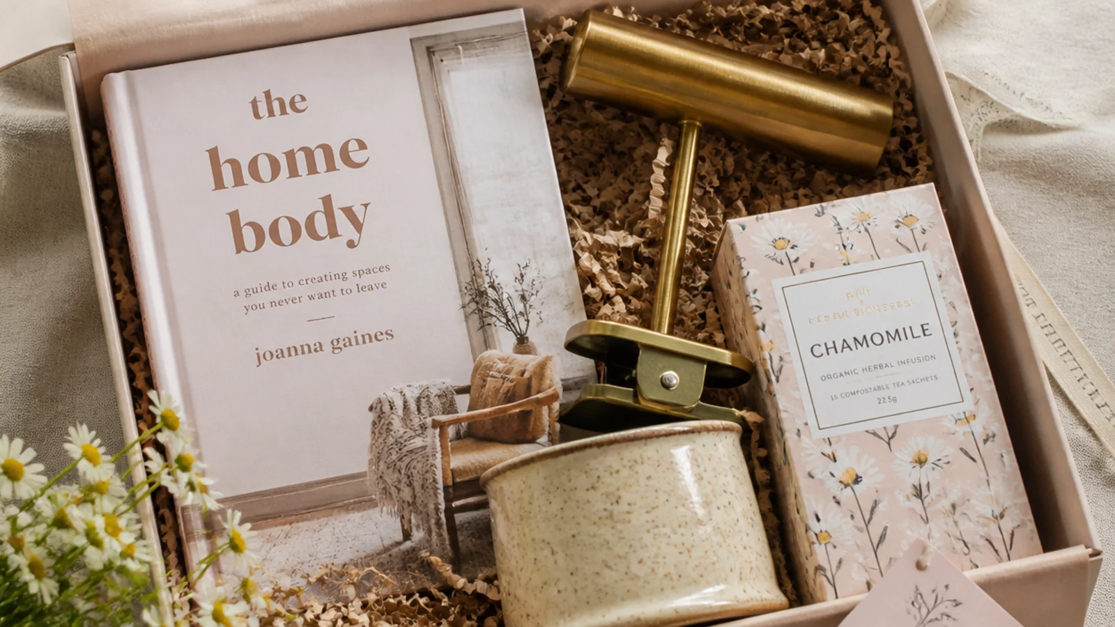 Faceless flat-lay of a book lover gift hamper with hardback, brass reading light and chamomile tea
