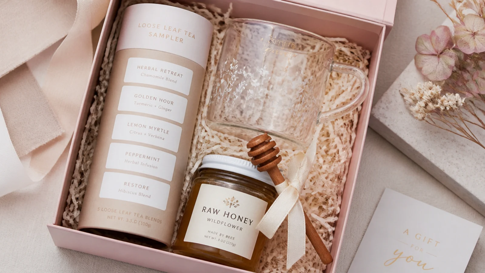 Faceless flat-lay of a tea ritual gift hamper with loose-leaf sampler, glass mug and raw honey