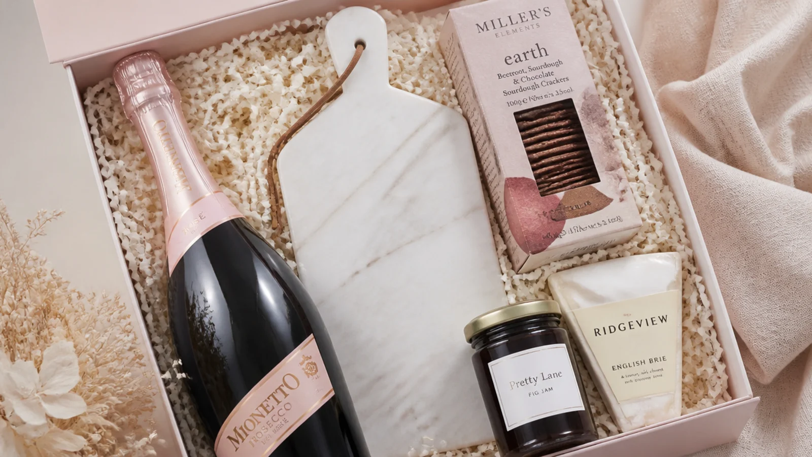 Faceless flat-lay of a wine and cheese gift hamper with prosecco, marble board and fig jam