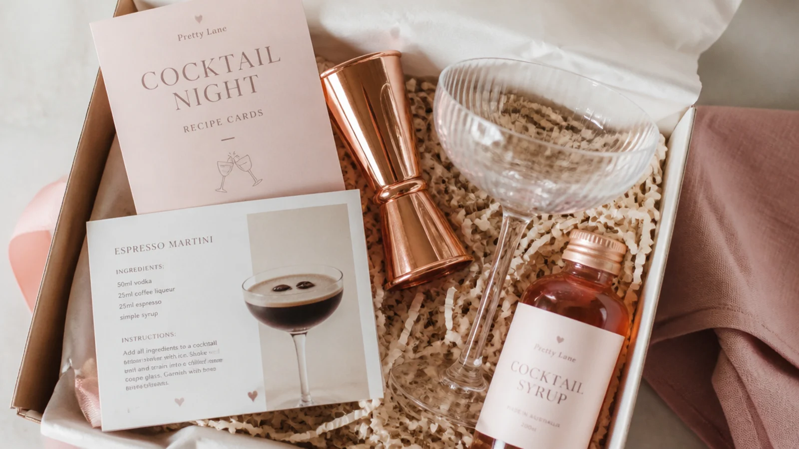 Faceless flat-lay of a cocktail night gift hamper with copper jigger, coupe glass and recipe cards