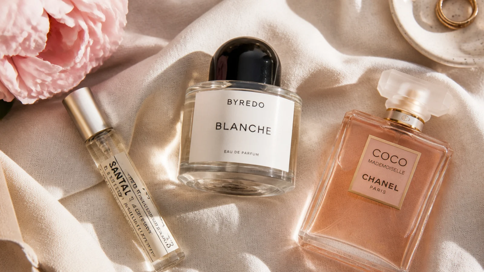 Faceless flat-lay of three fragrance bottles from rollerball to designer bottle on linen