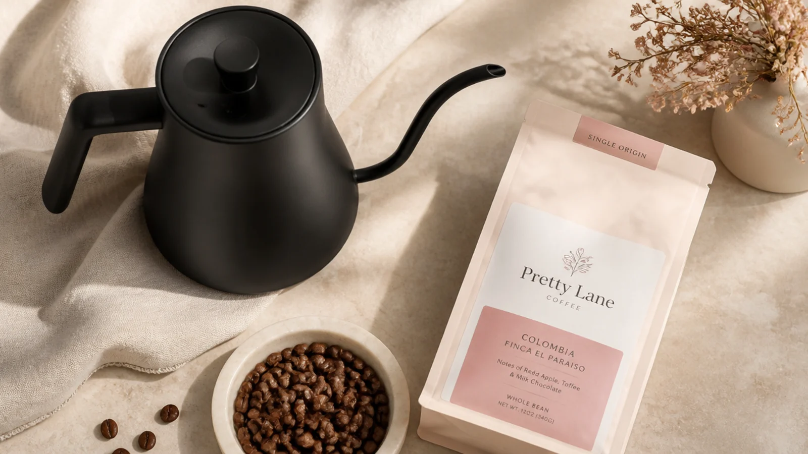 Faceless flat-lay of a matte black gooseneck pour-over kettle beside a bag of single-origin coffee beans