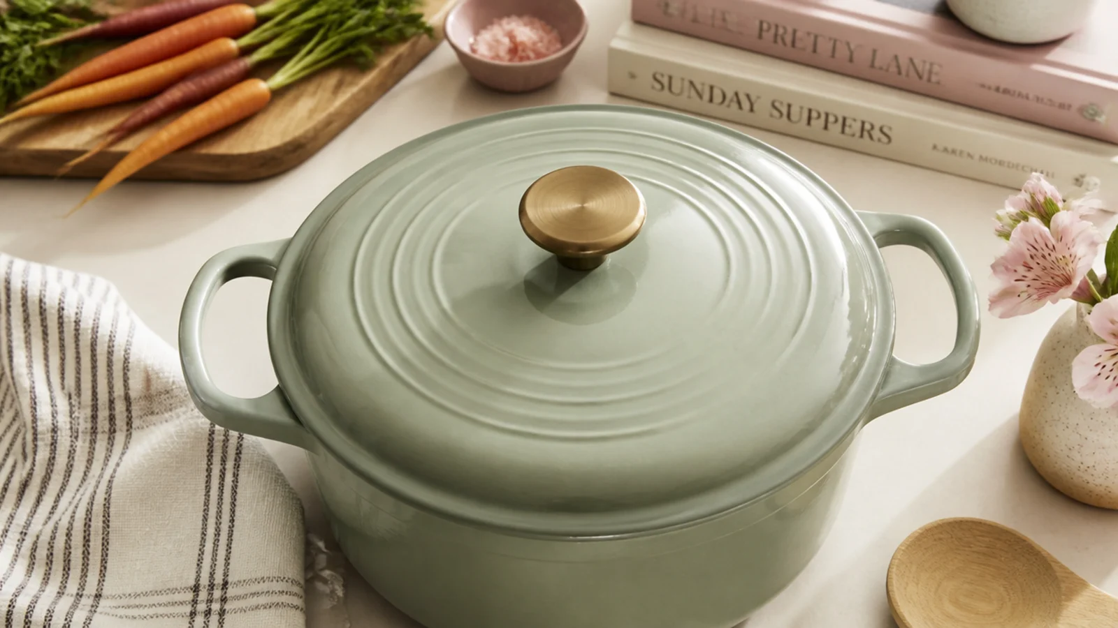 Faceless flat-lay of a sage green enameled cast-iron Dutch oven on a cream countertop