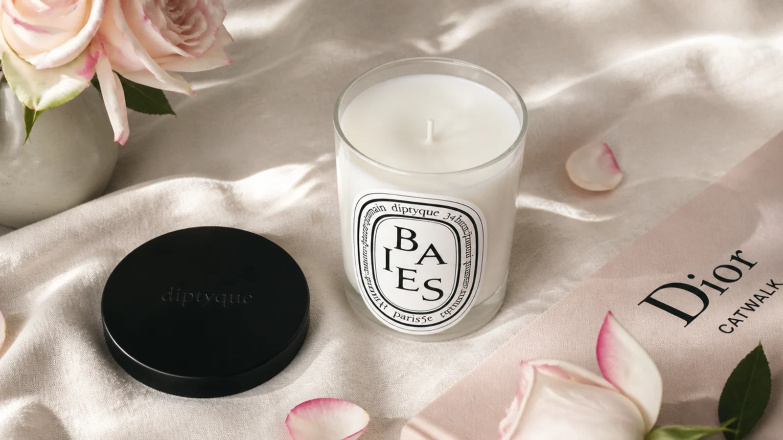 Faceless flat-lay of a Diptyque Baies candle in its glass vessel with the lid beside it on linen