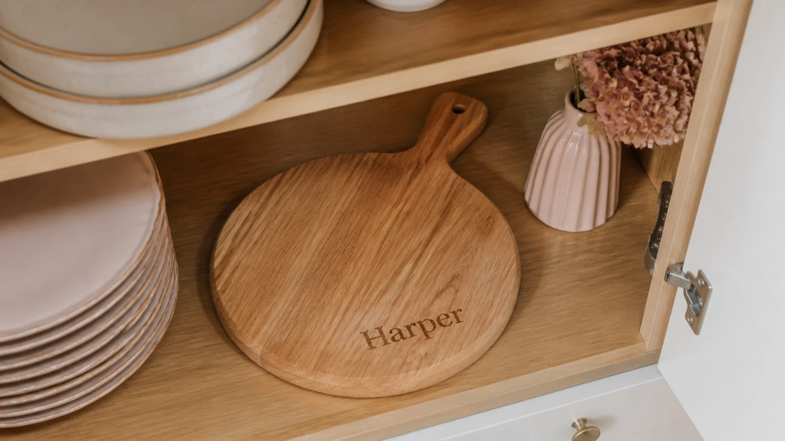 Faceless flat-lay of a wooden cutting board engraved with a name sitting unused in a cupboard