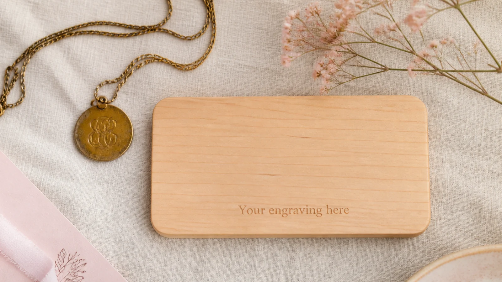 Faceless flat-lay contrasting a well-used gold necklace with an unused engraved board on linen