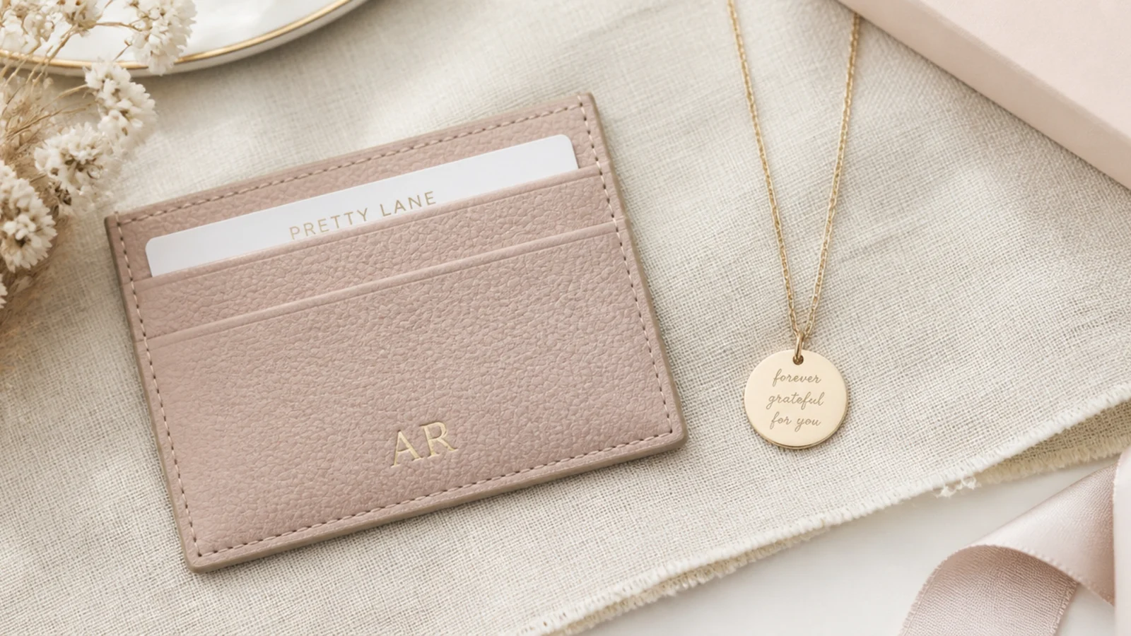 Faceless flat-lay comparing a practical leather cardholder and a sentimental engraved pendant on linen