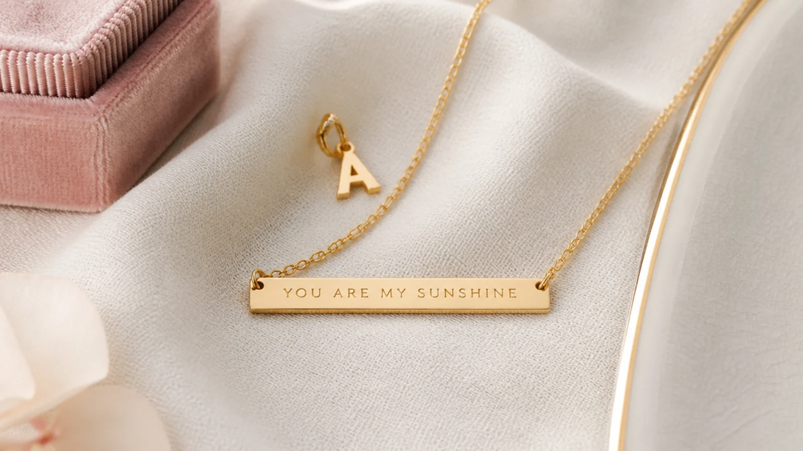 Faceless close flat-lay of an initial charm and an engraved bar necklace on a cream fabric surface