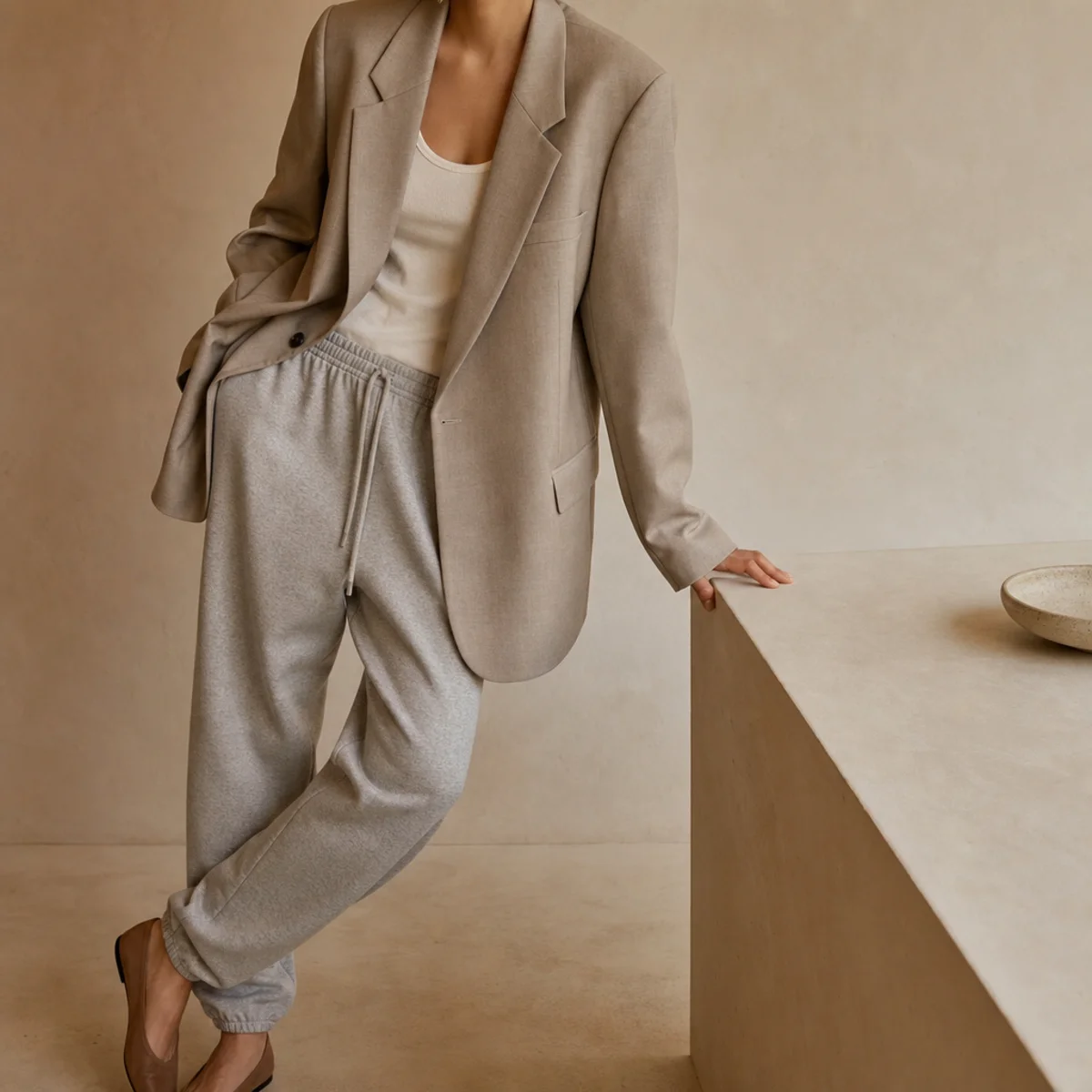 Faceless waist-up shot of an oversized neutral blazer over a tank with tapered grey sweatpants