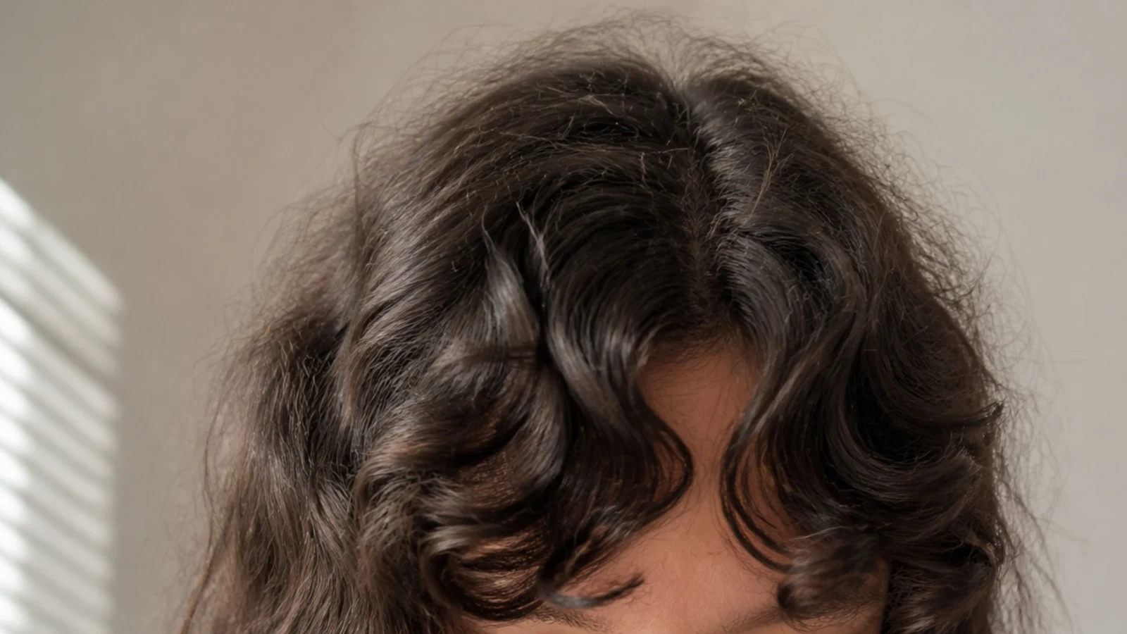 Curly curtain bangs on frizzy hair splitting at the center and softening into halo frizz